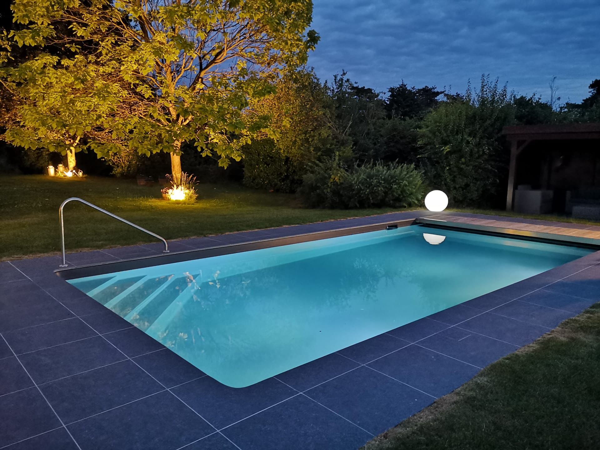 Piscine extérieure illuminée la nuit construite par Pool Plaisir